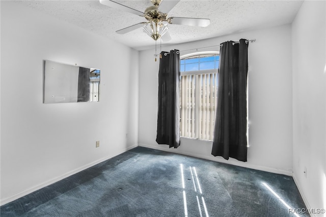 unfurnished room with ceiling fan, dark carpet, and a textured ceiling