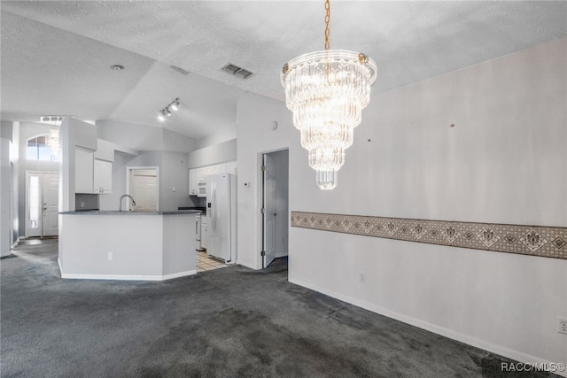 interior space featuring dark colored carpet, an inviting chandelier, white refrigerator with ice dispenser, vaulted ceiling, and white cabinets