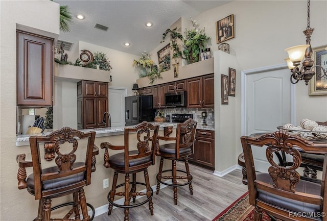 kitchen featuring light stone countertops, decorative backsplash, high vaulted ceiling, light hardwood / wood-style flooring, and black fridge