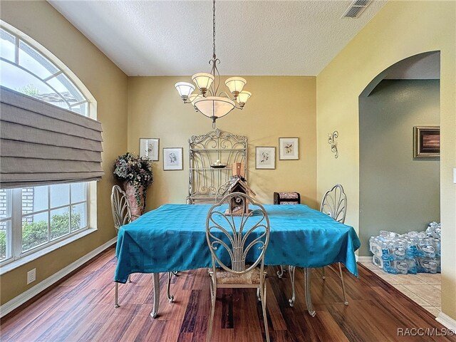 dining space featuring plenty of natural light, wood-type flooring, a textured ceiling, and a chandelier