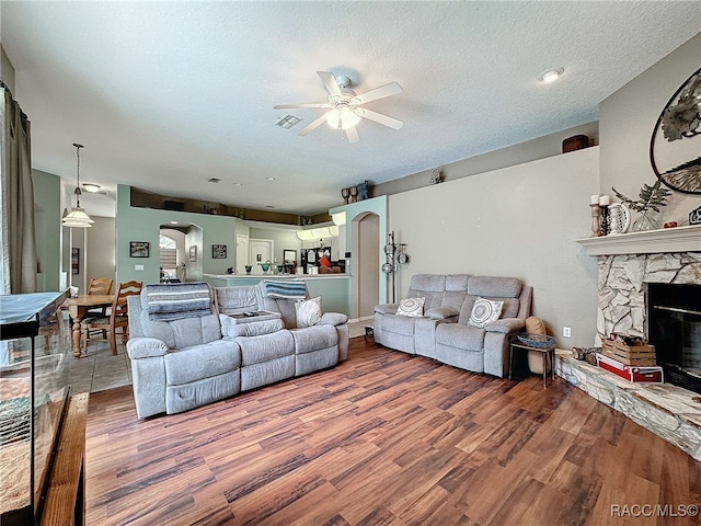 living room featuring a stone fireplace, ceiling fan, a textured ceiling, and hardwood / wood-style flooring