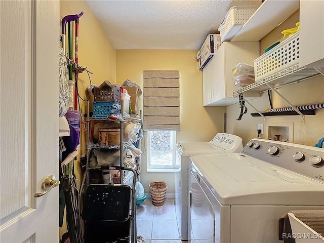 clothes washing area with cabinets, a textured ceiling, washing machine and dryer, and tile patterned floors