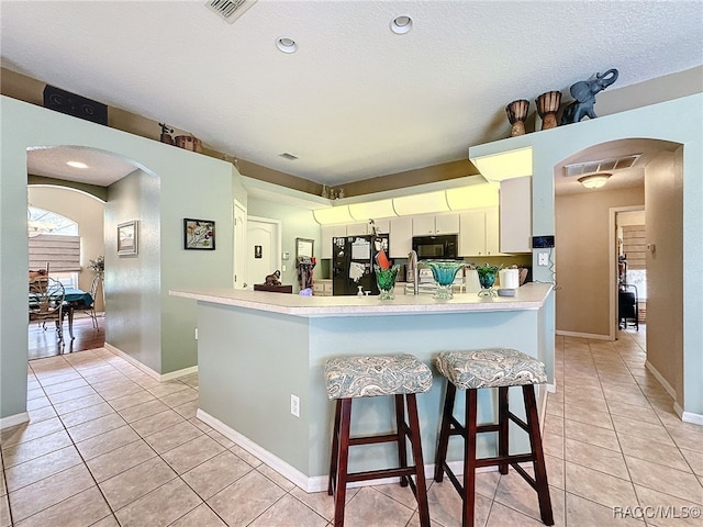 kitchen with kitchen peninsula, a kitchen breakfast bar, a textured ceiling, black appliances, and light tile patterned floors