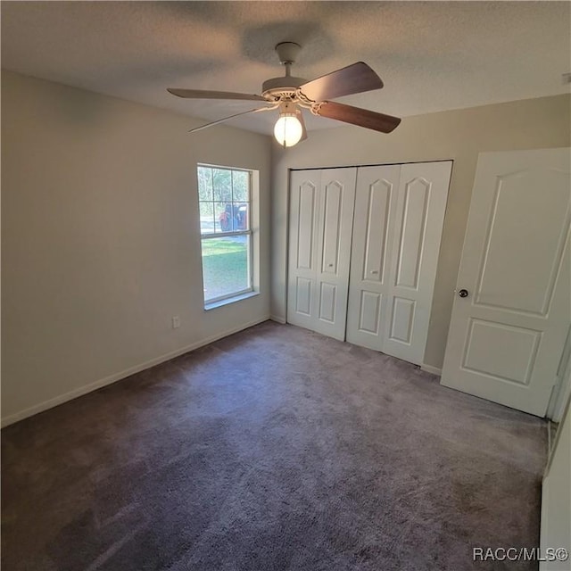 unfurnished bedroom with dark colored carpet, ceiling fan, a textured ceiling, and a closet