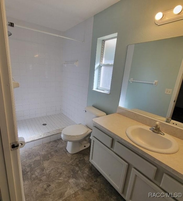 bathroom featuring a tile shower, vanity, and toilet