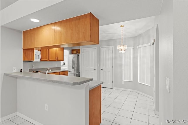 kitchen with decorative light fixtures, stainless steel fridge, a chandelier, light tile patterned floors, and kitchen peninsula