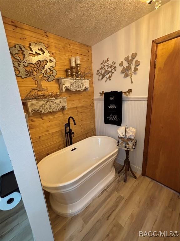4101 E Gloria Dr, Hernando, FL 34442 - bathroom with a soaking tub, wooden walls, a textured ceiling, wood finished floors, and wainscoting