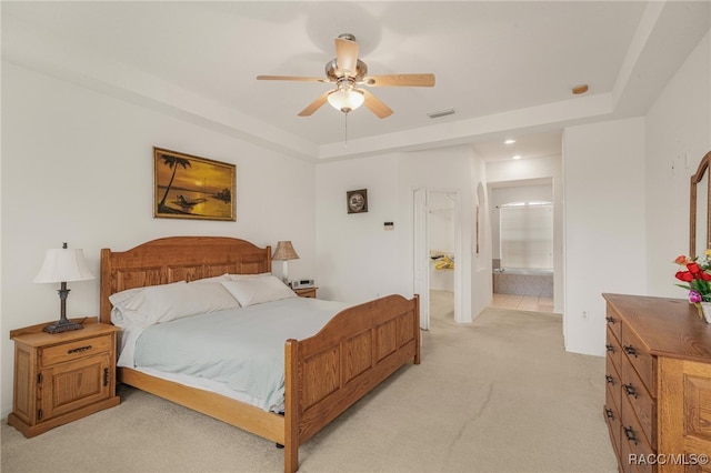 bedroom with a raised ceiling, light colored carpet, ceiling fan, and ensuite bath