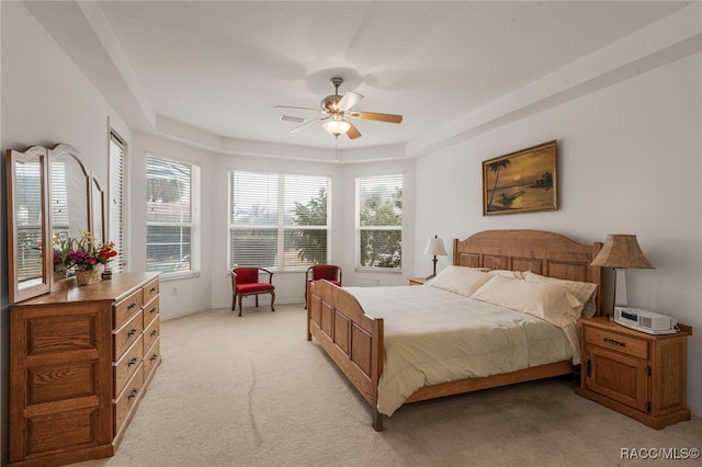 carpeted bedroom with a raised ceiling and ceiling fan