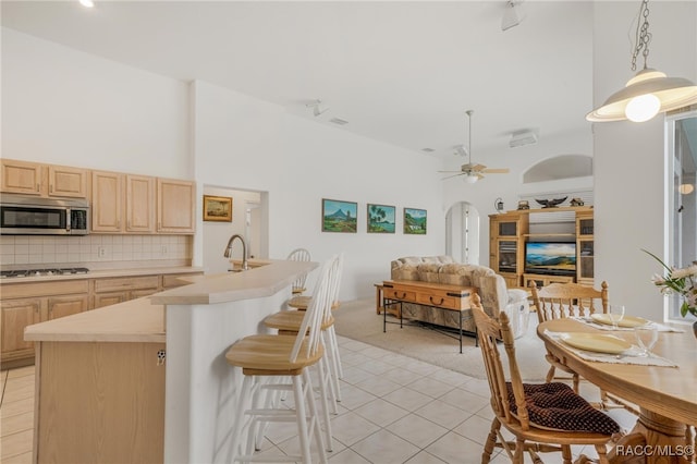 kitchen featuring gas cooktop, light brown cabinetry, decorative backsplash, and a towering ceiling