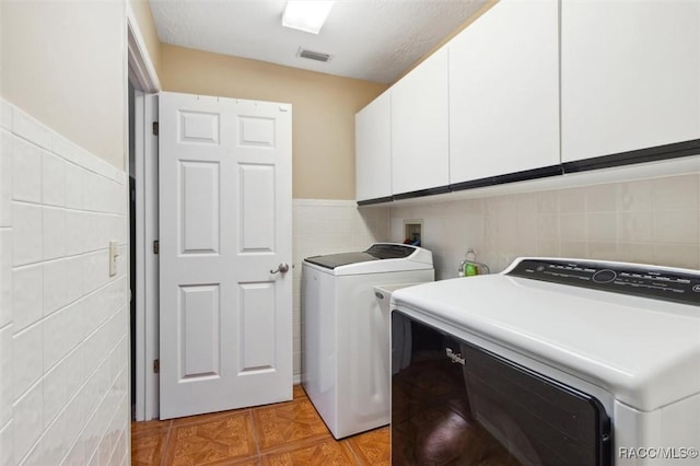 washroom with washer and dryer, cabinets, and tile walls