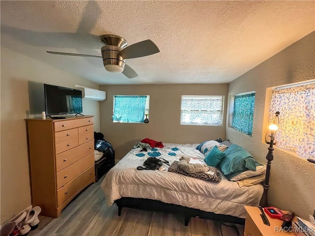 bedroom with ceiling fan, a wall mounted AC, hardwood / wood-style floors, vaulted ceiling, and a textured ceiling