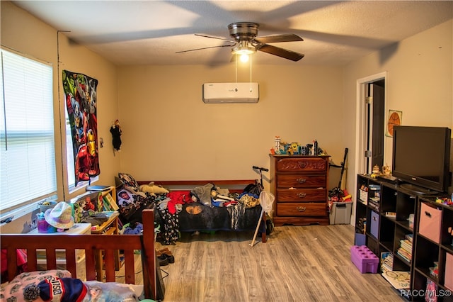 bedroom with a wall mounted air conditioner, light wood-type flooring, multiple windows, and ceiling fan