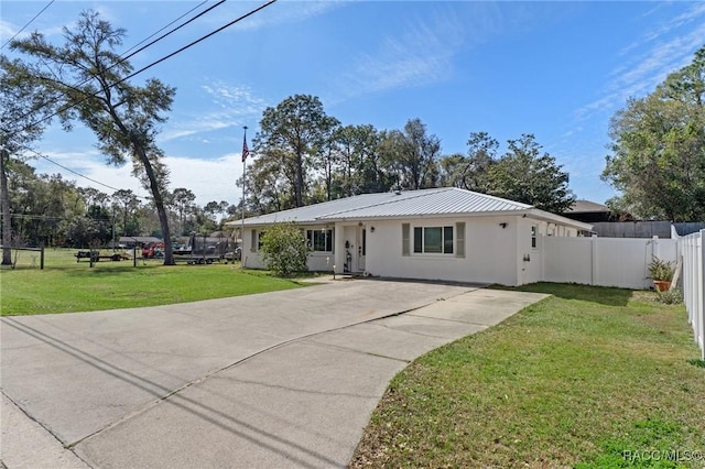 ranch-style home with metal roof, fence, driveway, stucco siding, and a front lawn