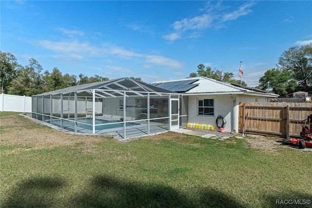 rear view of property with a fenced in pool, solar panels, glass enclosure, metal roof, and a fenced backyard