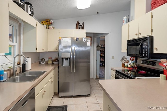 kitchen featuring cream cabinetry, light tile patterned floors, light countertops, appliances with stainless steel finishes, and a sink