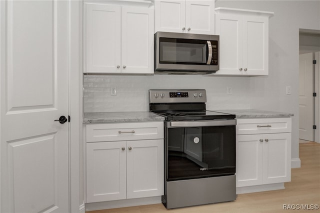 kitchen with light stone countertops, stainless steel appliances, backsplash, white cabinets, and light wood-type flooring