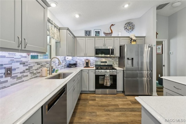 kitchen with appliances with stainless steel finishes, gray cabinets, lofted ceiling, and sink