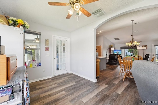 foyer entrance featuring ceiling fan with notable chandelier, vaulted ceiling, a textured ceiling, and dark wood-type flooring