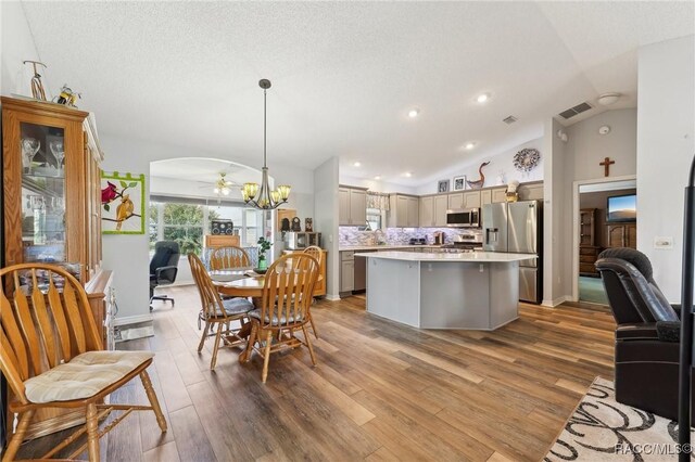 dining space with hardwood / wood-style flooring, ceiling fan with notable chandelier, lofted ceiling, and a textured ceiling