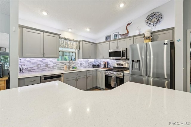 kitchen with tasteful backsplash, gray cabinetry, stainless steel appliances, vaulted ceiling, and sink