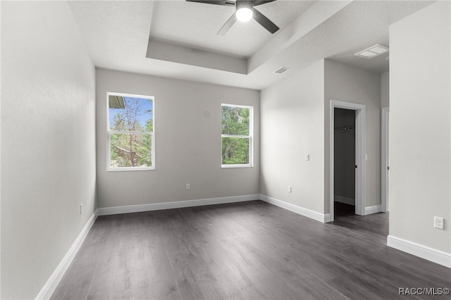 empty room with ceiling fan, a textured ceiling, dark hardwood / wood-style flooring, and a tray ceiling