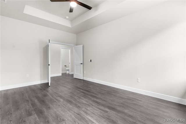 empty room with a tray ceiling, dark hardwood / wood-style floors, and ceiling fan