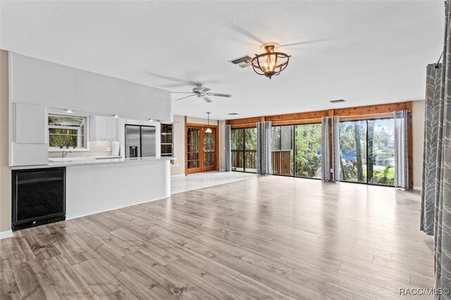 unfurnished living room featuring wine cooler, ceiling fan, and light wood-type flooring