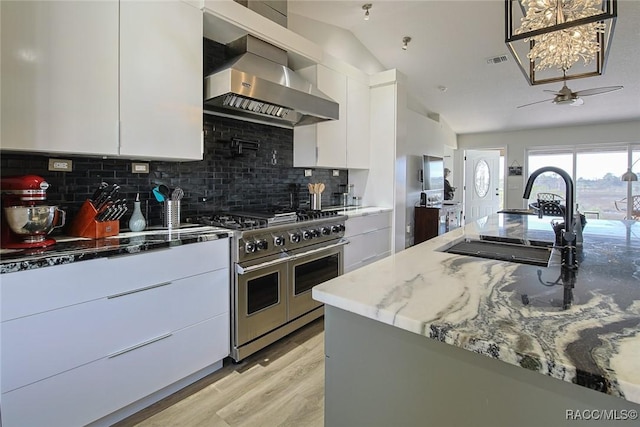 kitchen featuring wall chimney exhaust hood, sink, stone countertops, double oven range, and white cabinets