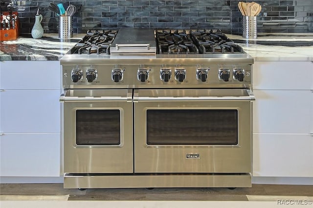 interior details with light stone counters, tasteful backsplash, white cabinetry, and range with two ovens