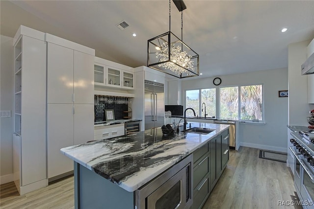 kitchen featuring white cabinetry, an island with sink, built in appliances, and dark stone counters