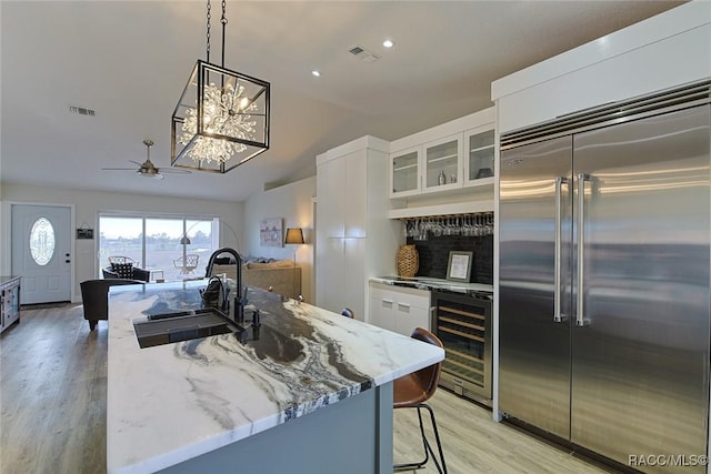 kitchen with built in refrigerator, beverage cooler, sink, and white cabinets