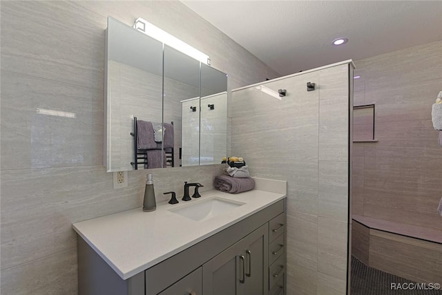 bathroom with a tile shower, vanity, and tile walls