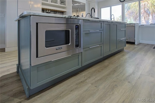 kitchen with gray cabinets, stainless steel built in refrigerator, sink, and light wood-type flooring