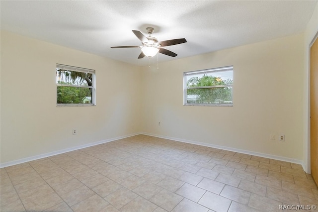 empty room with a wealth of natural light, ceiling fan, light tile patterned flooring, and a textured ceiling