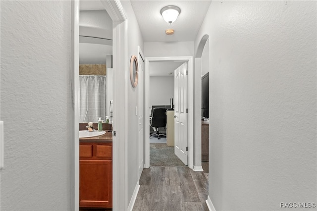 hall with a textured wall, dark wood-style flooring, a sink, and baseboards