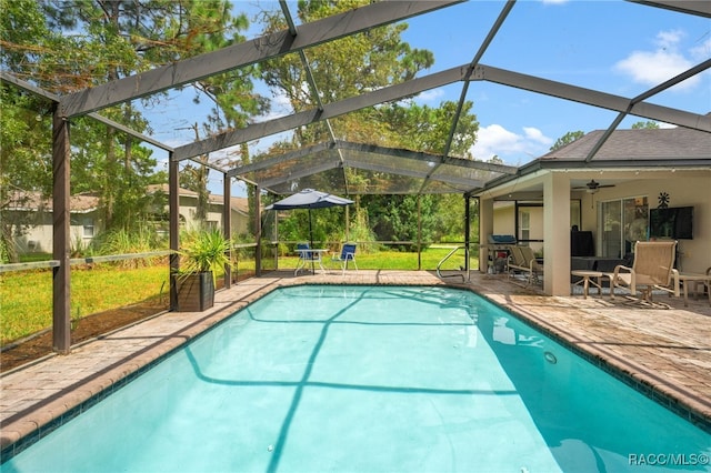 outdoor pool with a patio area, ceiling fan, glass enclosure, and a yard