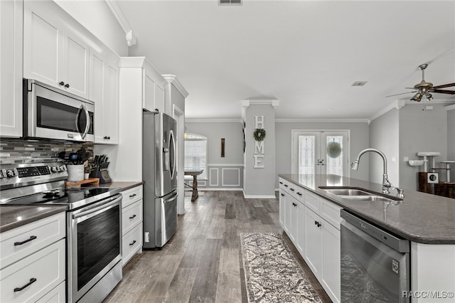 kitchen with ornamental molding, wood finished floors, a kitchen island with sink, stainless steel appliances, and a sink