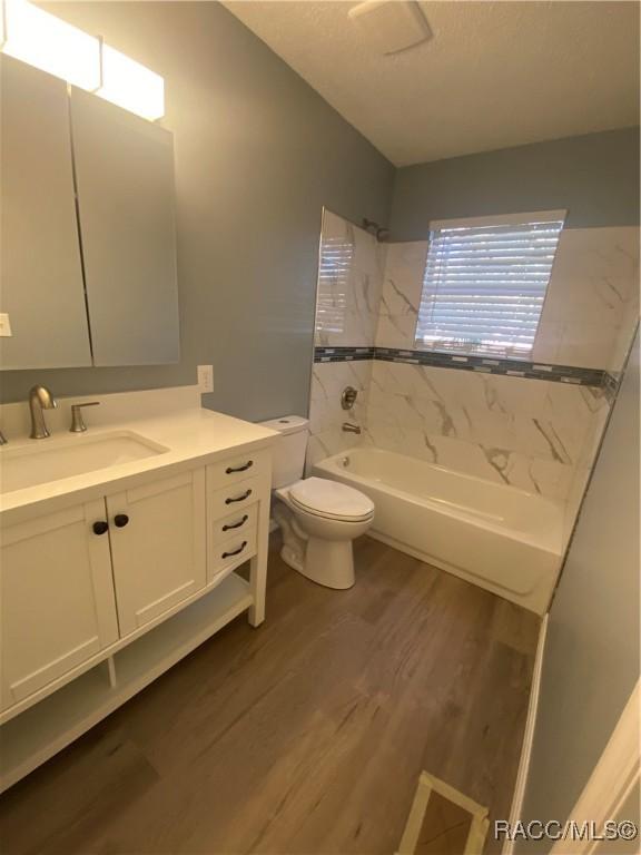 full bathroom with vanity, wood-type flooring, tiled shower / bath combo, and toilet