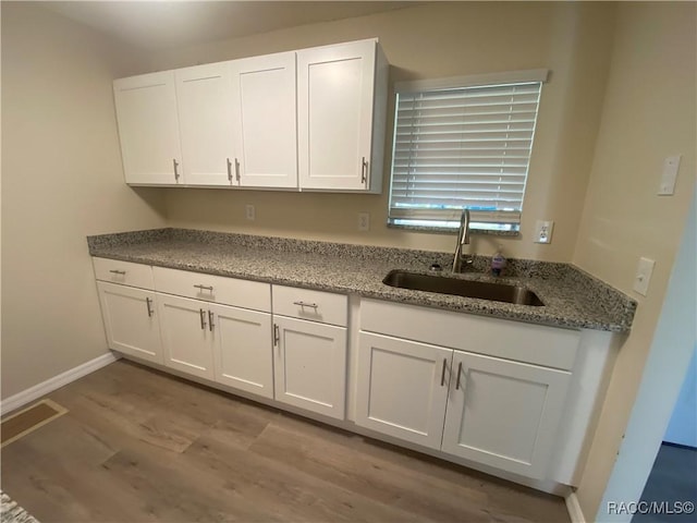 kitchen featuring white cabinetry, sink, stone countertops, and light hardwood / wood-style flooring