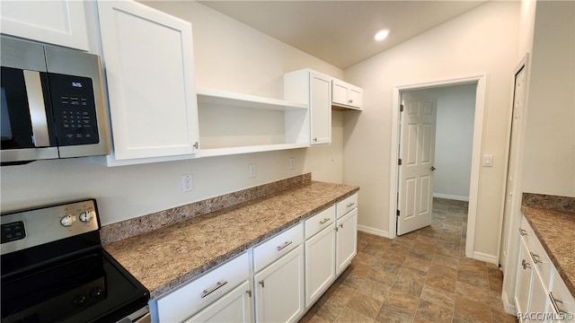 kitchen with light stone countertops, appliances with stainless steel finishes, white cabinetry, and lofted ceiling