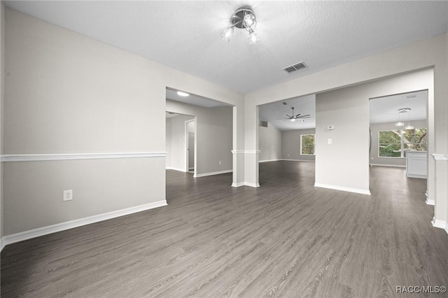 unfurnished room with a textured ceiling, ceiling fan with notable chandelier, and dark wood-type flooring