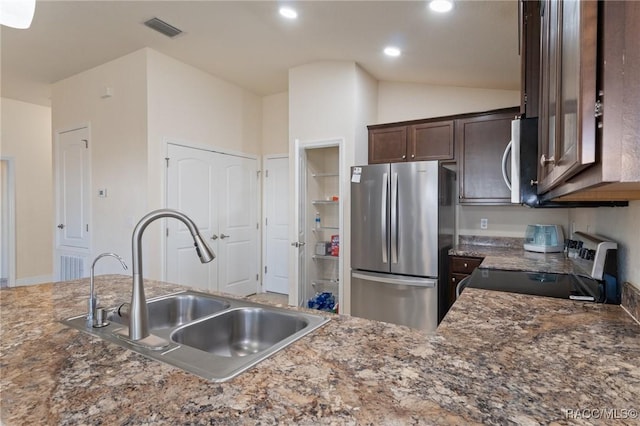 kitchen featuring vaulted ceiling, sink, dark stone countertops, stainless steel appliances, and dark brown cabinets