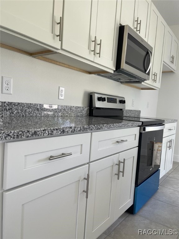 kitchen featuring light tile patterned flooring, dark stone countertops, white cabinetry, and appliances with stainless steel finishes