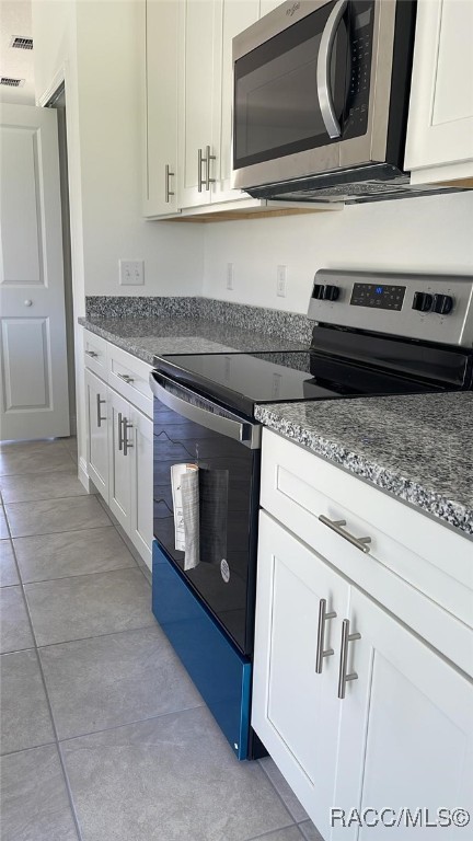 kitchen featuring white cabinets, stone countertops, light tile patterned flooring, and appliances with stainless steel finishes