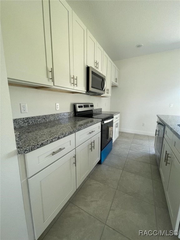 kitchen featuring tile patterned floors, dark stone countertops, white cabinetry, and appliances with stainless steel finishes