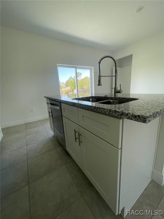 kitchen featuring dishwasher, a kitchen island with sink, sink, stone countertops, and white cabinetry