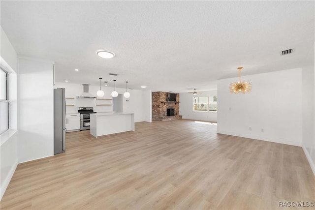 unfurnished living room with a brick fireplace, ceiling fan with notable chandelier, a textured ceiling, and light hardwood / wood-style floors