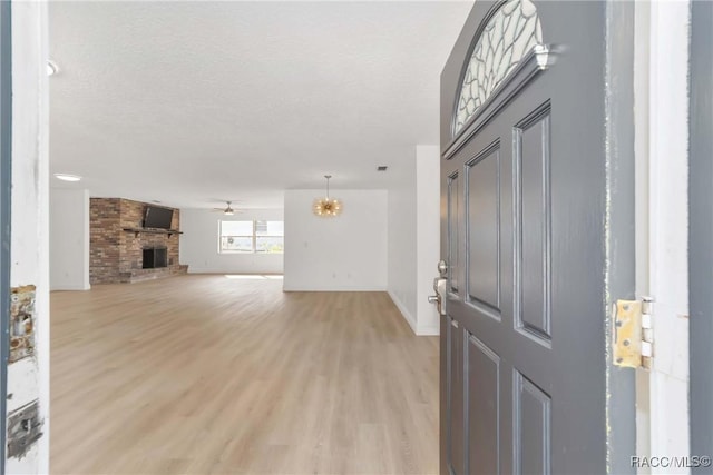 foyer with ceiling fan with notable chandelier, light wood-type flooring, a brick fireplace, and a textured ceiling