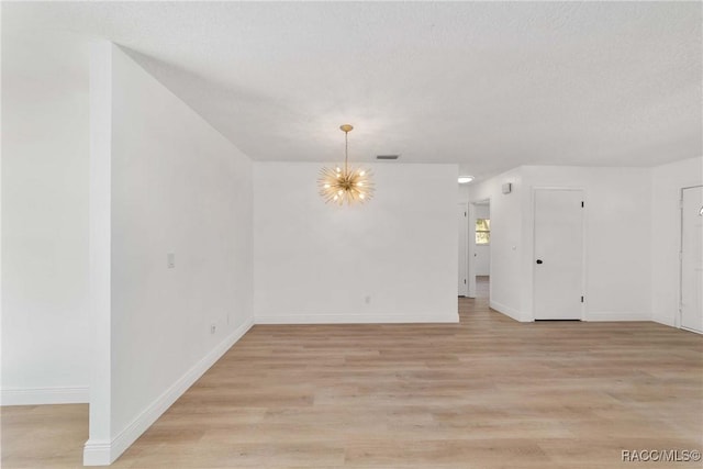 empty room featuring a notable chandelier, light hardwood / wood-style floors, and a textured ceiling